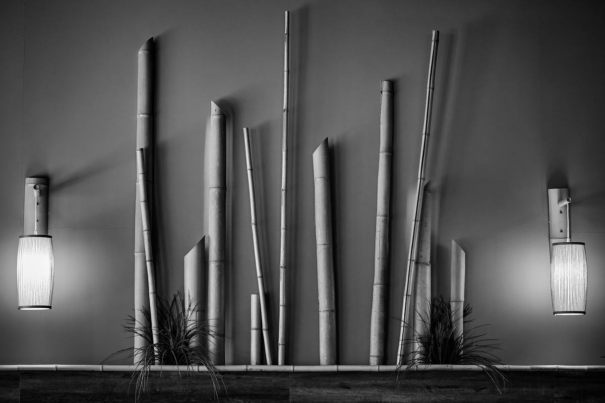 A wall installation of bamboo stalks lit by paper lantern sconces.