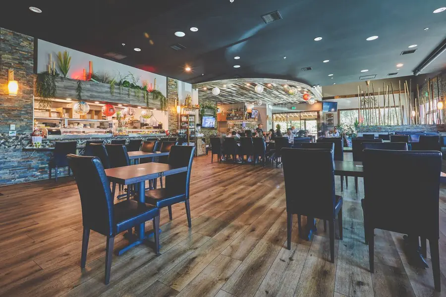The Misaka dining room — dark wood tables and chairs facing the sushi bar under warm lighting.