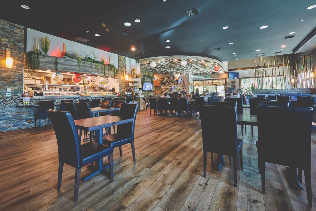 The Misaka dining room — dark wood tables and chairs facing the sushi bar under warm lighting.